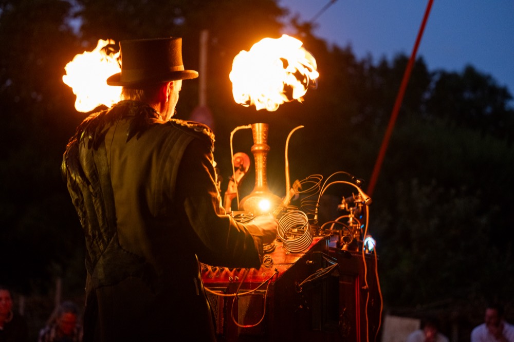 Flames bursting from the machine behind Hjalte in his top hat
